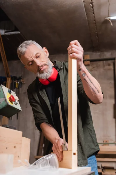 Carpinteiro tatuado verificando prancha de madeira no estúdio de madeira — Fotografia de Stock
