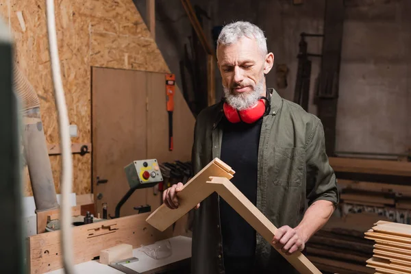 Mature concepteur de meubles barbus tenant des planches en bois dans le studio de menuiserie — Photo de stock