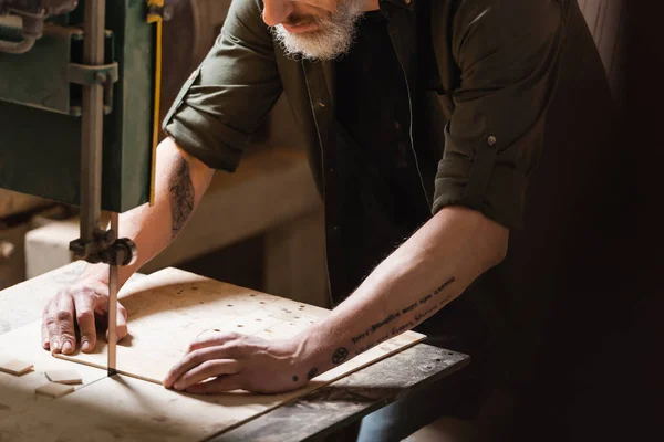 Partial view of tattooed woodworker cutting plywood with band saw — Stock Photo