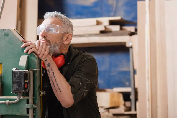 Продуманий дизайнер меблів в окулярах дивиться далеко в деревообробну студію — стокове фото