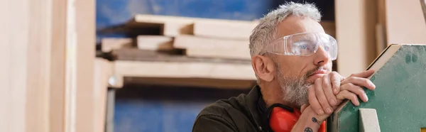 Pensive grey haired furniture designer in goggles looking away in workshop, banner — Stock Photo