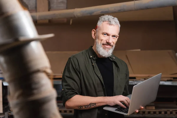 Tattooed furniture designer with laptop smiling at camera on blurred foreground — Stock Photo