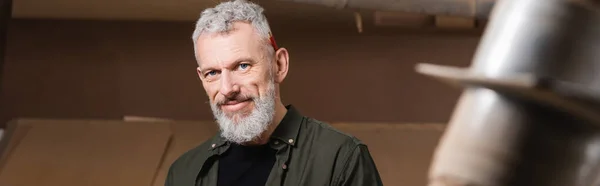 Happy bearded furniture designer looking at camera in woodwork studio, banner — Stock Photo