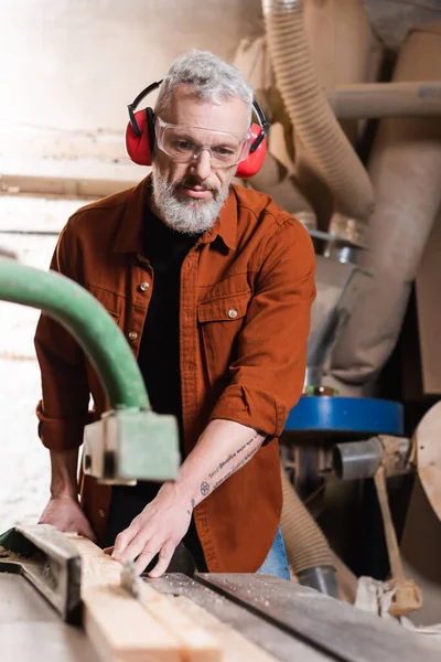 Плотник средних лет, работающий на размытой столярной машине в мастерской — стоковое фото
