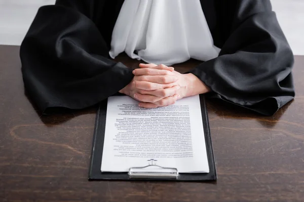 Cropped view of judge with clenched hands near lawsuit on desk - foto de stock