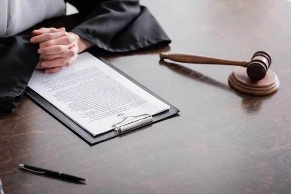 Partial view of prosecutor with clenched hands near lawsuit and gavel on wooden desk — Stock Photo