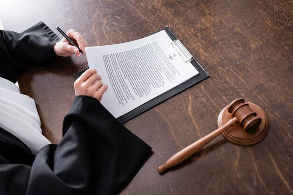 Cropped view of judge signing verdict near wooden gavel on desk — стоковое фото