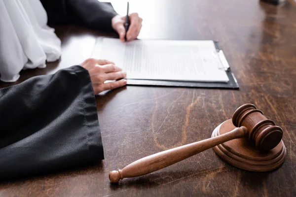 Selective focus of wooden gavel near cropped judge signing verdict on blurred background — Foto stock