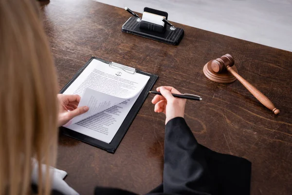 Partial view of blurred prosecutor holding pen near lawsuit and wooden gavel — Stock Photo