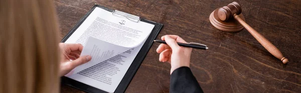 Cropped view of blurred judge with pen near lawsuit and wooden gavel on desk, banner - foto de stock