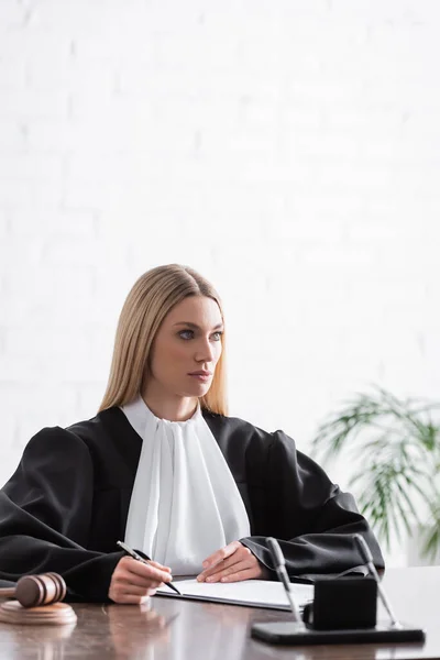 Blonde prosecutor holding pen and looking away at workplace — Foto stock