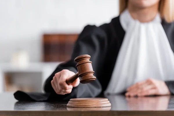 Partial view of blurred judge in mantle holding wooden gavel — Fotografia de Stock