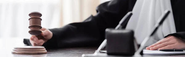 Cropped view of judge with gavel near burred pens on desk, banner — Fotografia de Stock