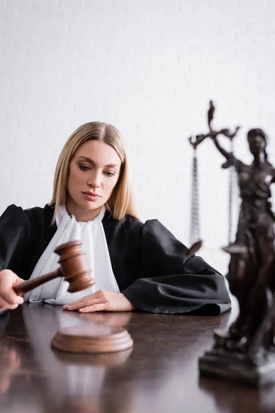 Judge holding gavel near blurred themis statue on desk — Stockfoto