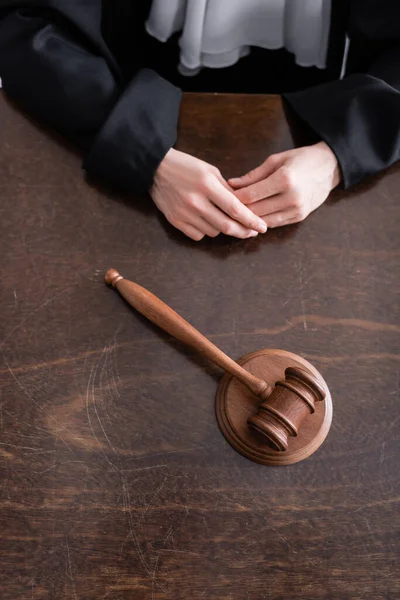 Partial view of judge sitting near wooden gavel on desk — стоковое фото