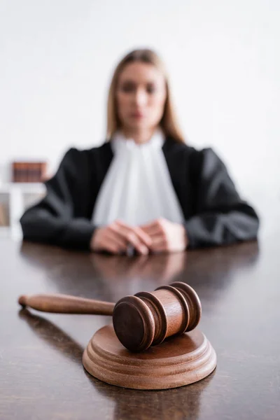 Selective focus of wooden gavel near blurred prosecutor sitting at desk in black mantle — Fotografia de Stock