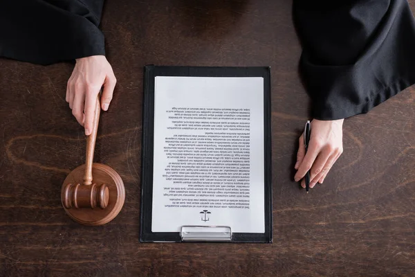 Top view of cropped judge with wooden gavel and pen near clipboard with verdict — Stock Photo