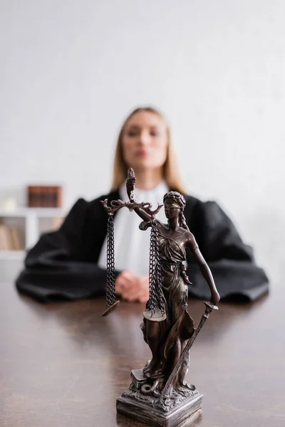 Enfoque selectivo de themis estatua cerca de fiscal en manto negro sentado sobre fondo borroso - foto de stock