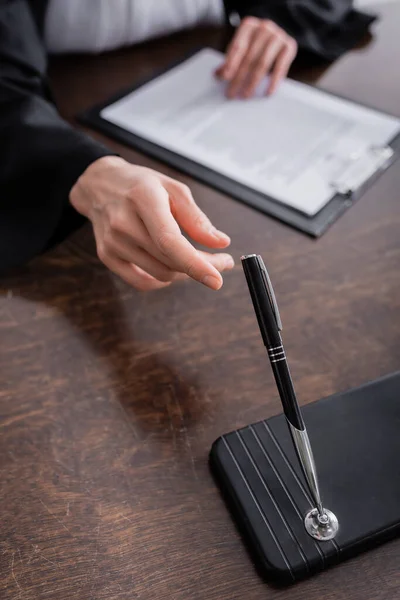 Abgeschnittene Ansicht des Staatsanwalts, der Stift nimmt, während er in der Nähe des unscharfen Klemmbretts sitzt — Stockfoto