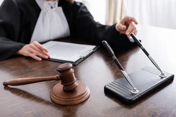 Selective focus of wooden gavel and pens near cropped judge on blurred background — Fotografia de Stock