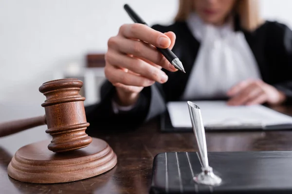 Selective focus of wooden gavel near cropped prosecutor with pen on blurred background — Photo de stock