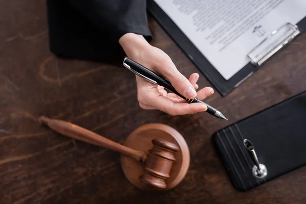 Top view of cropped prosecutor holding pen near gavel and clipboard on wooden desk — Stock Photo