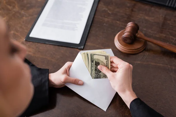 Partial view of prosecutor with bribe in envelope near blurred gavel on desk — Stock Photo