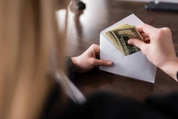 Partial view of prosecutor holding envelope and dollar banknotes on blurred foreground — Stock Photo