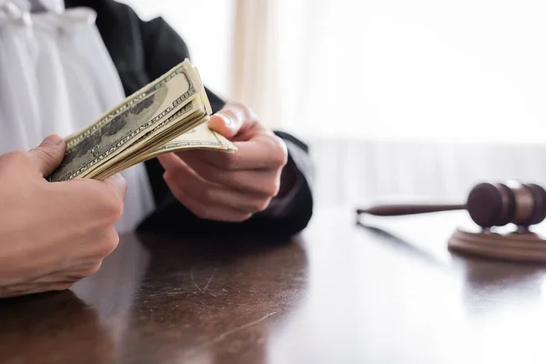 Partial view of prosecutor counting dollar banknotes near blurred gavel — Stock Photo