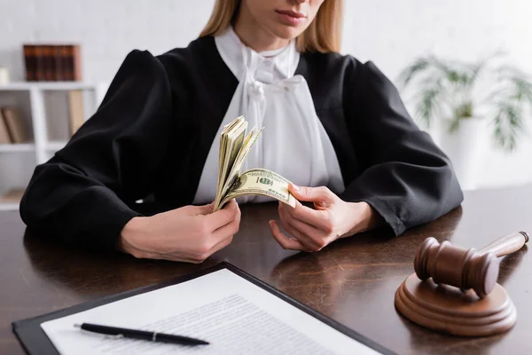 Partial view of prosecutor counting dollar banknotes near gavel and lawsuit on desk — Stock Photo