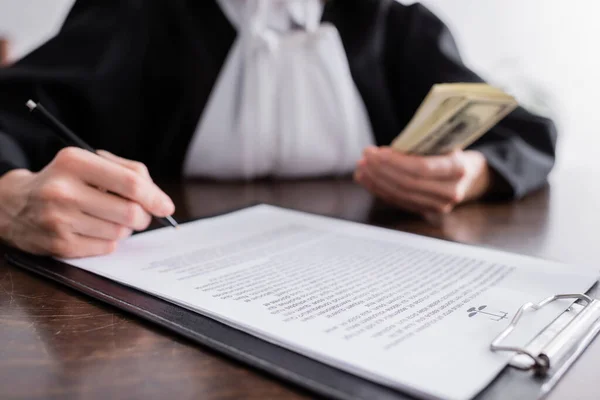 Ausgeschnittene Ansicht des verschwommenen Staatsanwalts mit Stift und Geld in der Nähe des Prozesses auf Klemmbrett — Stockfoto