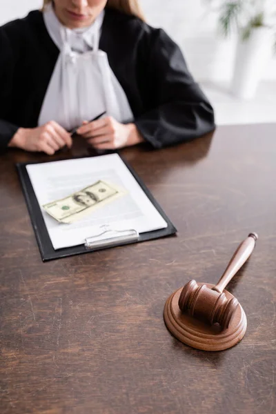 Selective focus of gavel near lawsuit, dollars and cropped judge on blurred background — Stockfoto