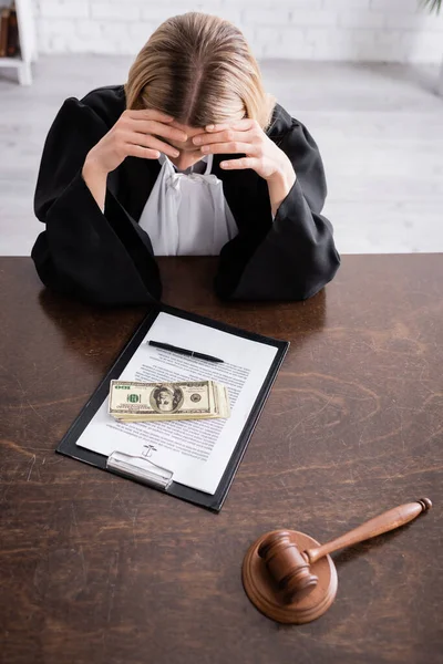 High angle view of prosecutor sitting with bowed head near dollars and lawsuit on clipboard - foto de stock