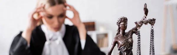 Selective focus of themis statue near thoughtful prosecutor touching head on blurred background, banner — Stock Photo