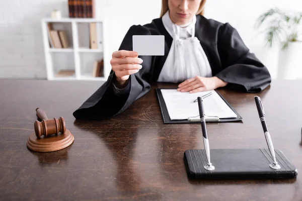 Cropped view of prosecutor showing blank business card while sitting near lawsuit and gavel — Stock Photo