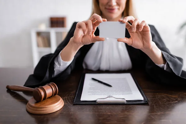 Cropped view of smiling prosecutor holding empty business card near clipboard and wooden gavel — Photo de stock