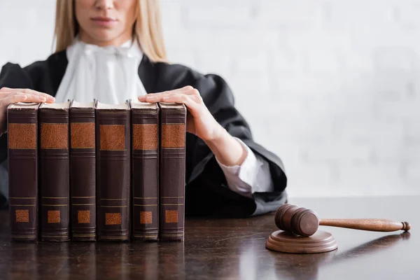 Partial view of prosecutor sitting near collection of books and wooden gavel on desk - foto de stock