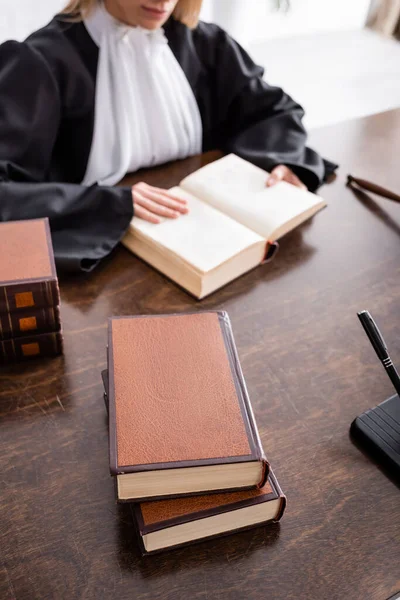 Vista recortada del fiscal borroso leyendo literatura jurídica cerca de libros en escritorio de madera - foto de stock