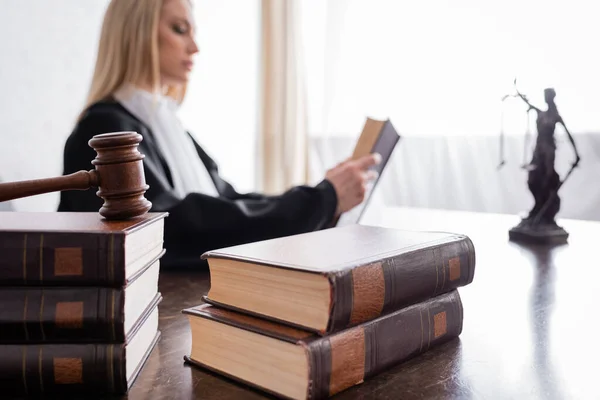 Collection of books and gavel near prosecutor reading on blurred background — Photo de stock
