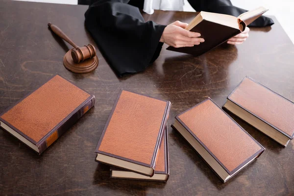 Partial view of prosecutor reading book near collection of literature on desk — Stock Photo