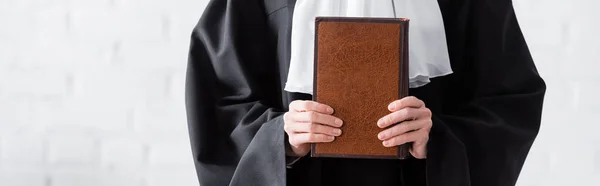 Cropped view of judge in black mantle holding book, banner — Stock Photo