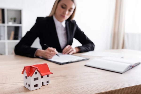 Selective focus of house model and blurred notary signing contract on blurred background — Fotografia de Stock