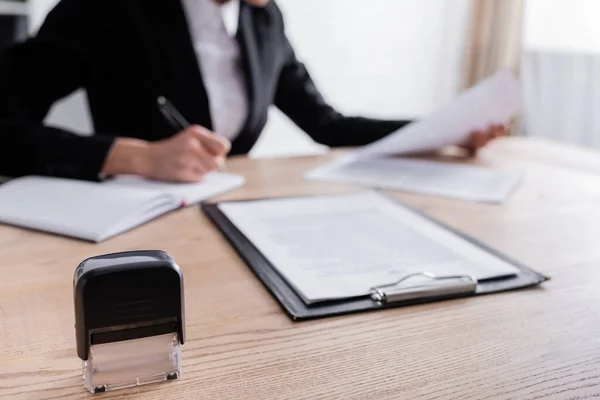 Selective focus of stamper and clipboard near cropped notary writing on blurred background — Fotografia de Stock