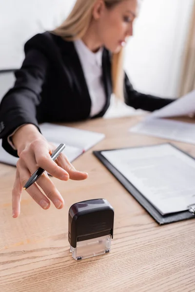 Lawyer reaching stamper while working with documents on blurred background — Stock Photo