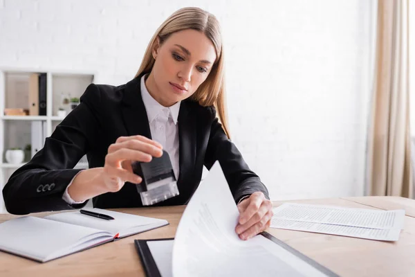 Notaio biondo con timbro mentre lavora con i documenti in ufficio — Foto stock