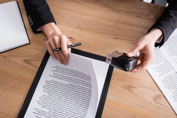 Partial view of notary holding stamper and pen near documents on wooden desk — Photo de stock