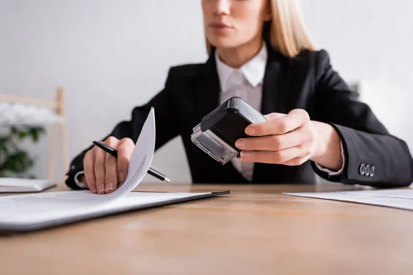 Partial view of lawyer with pen and stamper working with contract on blurred background — Fotografia de Stock