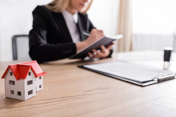 Cropped view of notary writing near house model on blurred foreground — Fotografia de Stock