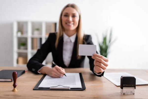 Happy notary holding blank business card while sitting on blurred background — Foto stock