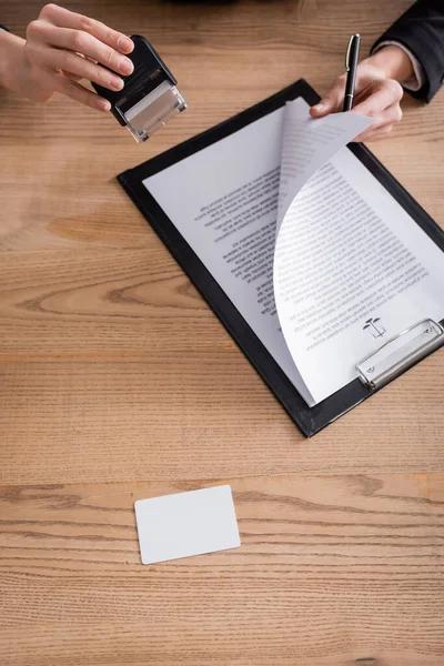 Top view of contract and blank business card near cropped notary with stamper and pen — Stockfoto